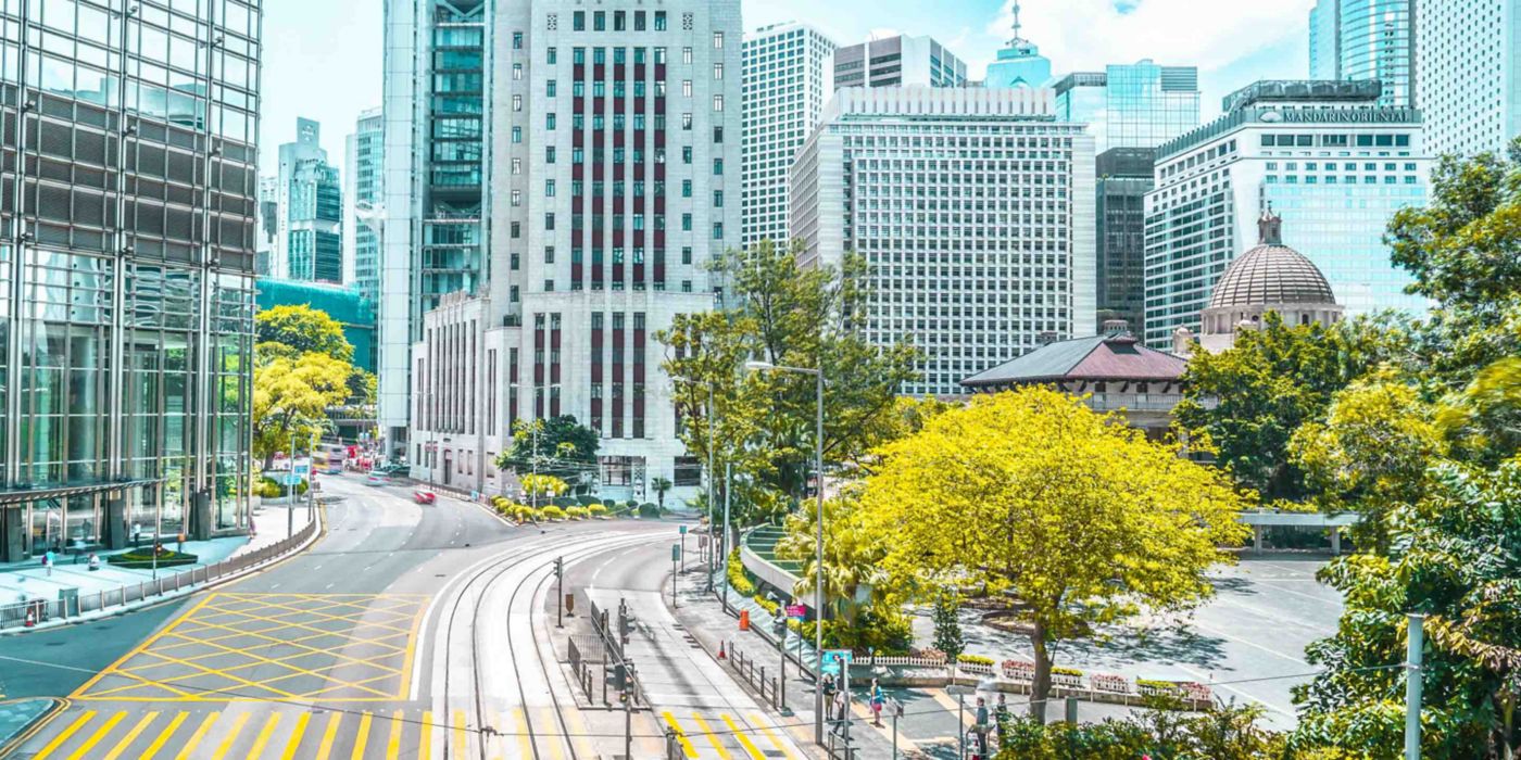 Discover a vibrant urban scene featuring towering modern buildings, a gracefully curved road, and lush greenery lining the sidewalks. This cityscape captures the dynamic blend of architecture and nature in contemporary city planning.