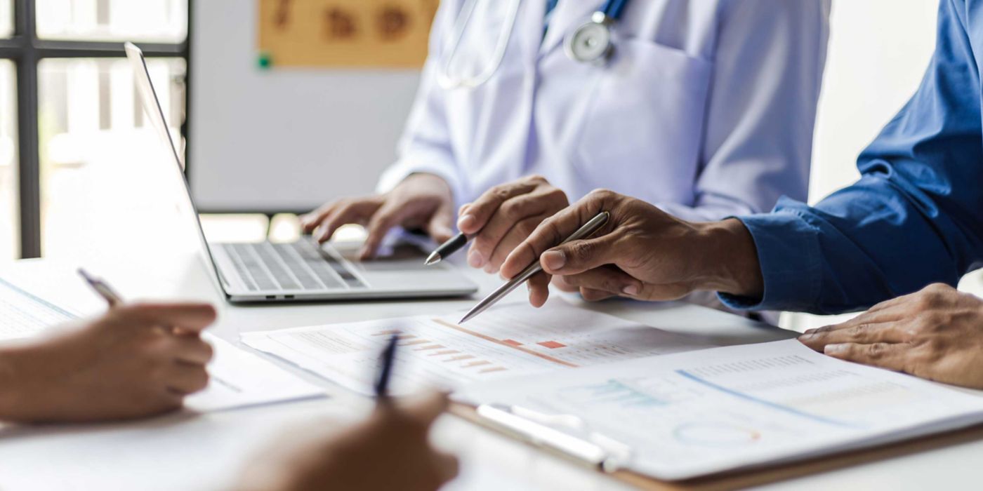 Team, medical analysts and doctors consulting with paperwork of graphs, data and charts in hospital conference room. Healthcare staff discussing statistics, results of research and innovation.
