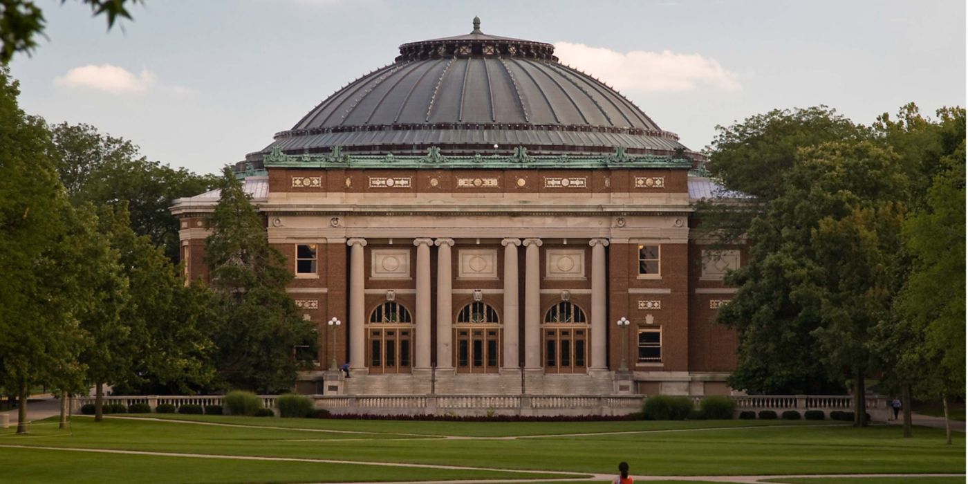Brick building with dome, columns, trees, and green lawn.