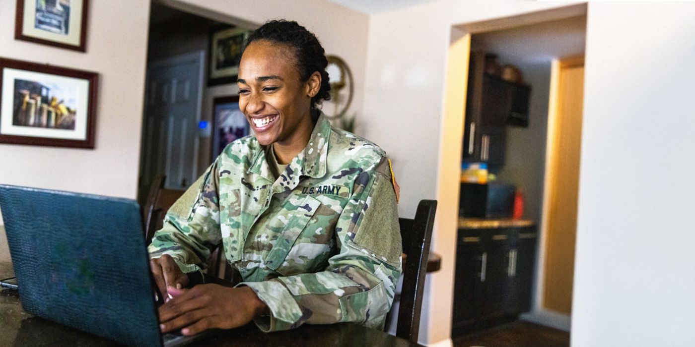 Soldier in uniform works remotely from home using laptop.