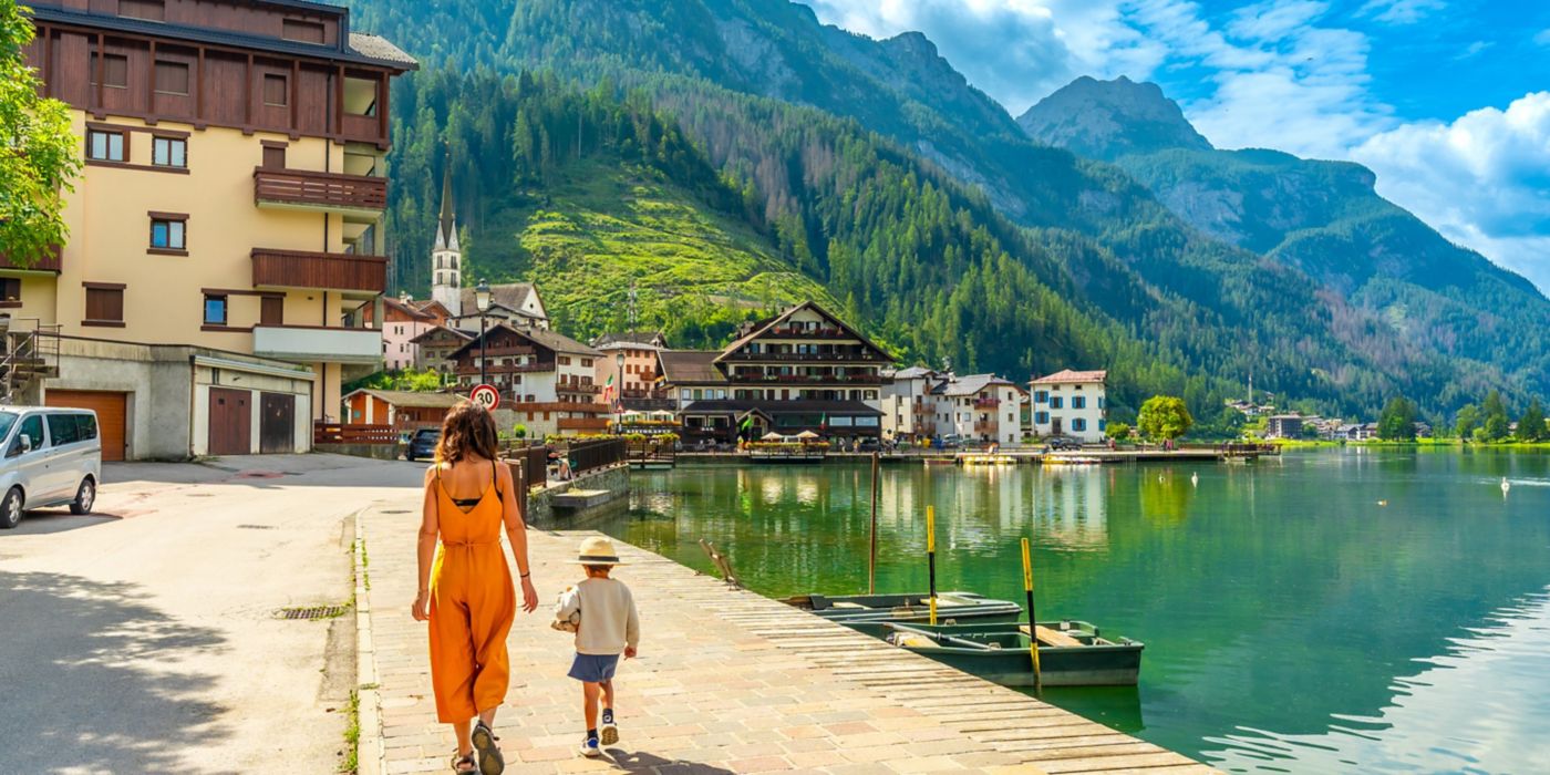 Woman and child stroll beside scenic lakeside mountain town.