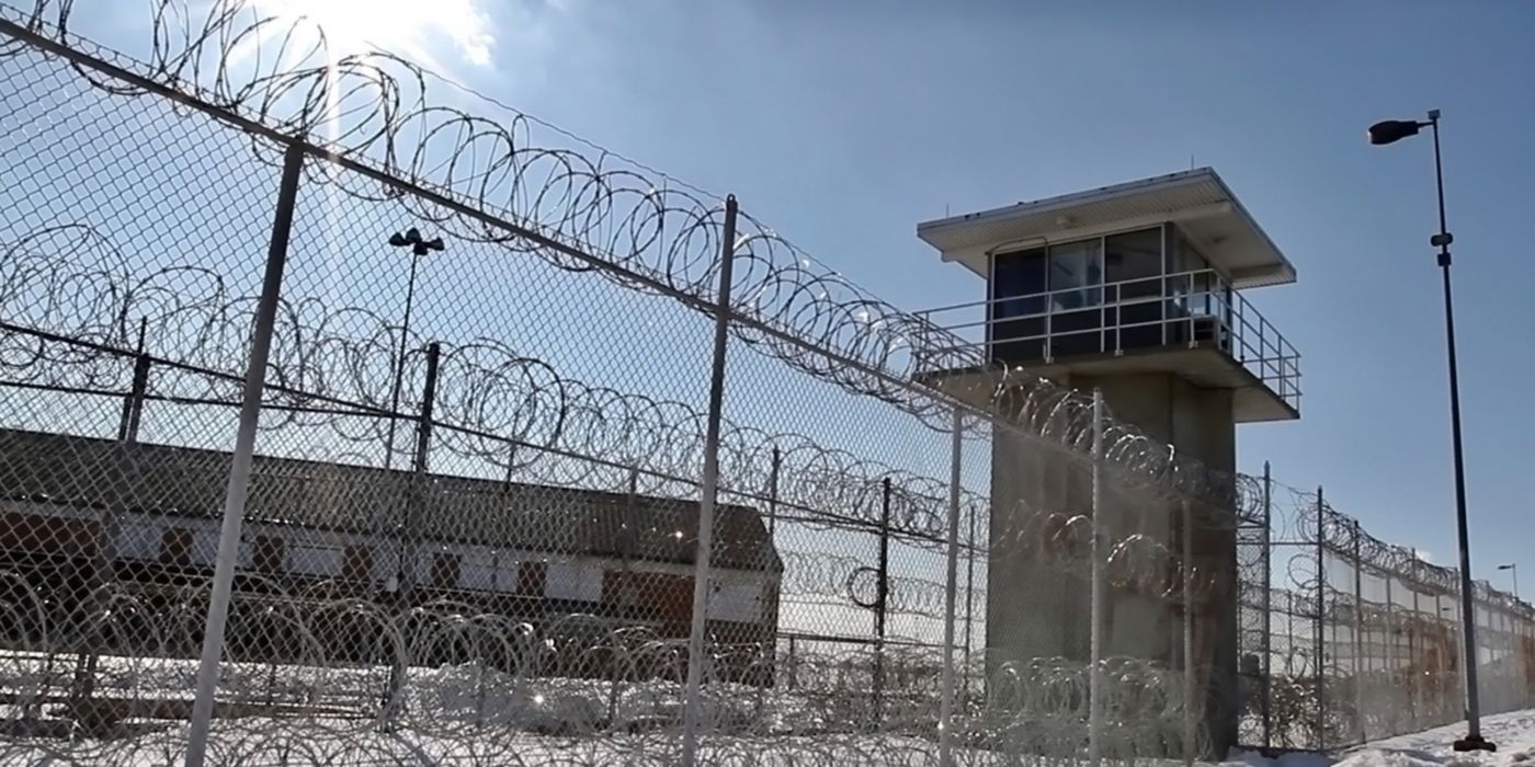 Barbed wire fence surrounds tower under clear sky, lights visible.