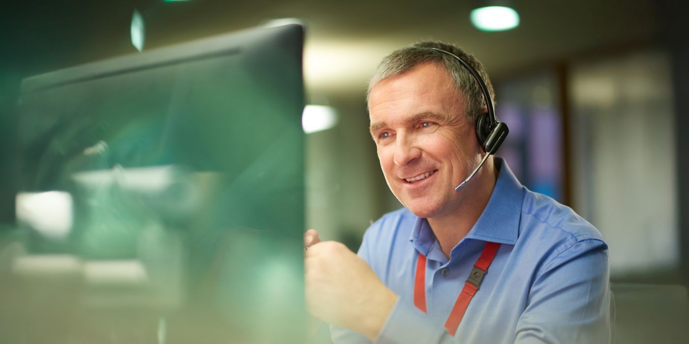 Person wearing a headset seated at a desk and viewing a computer monitor in an office environment with blurred background lighting.