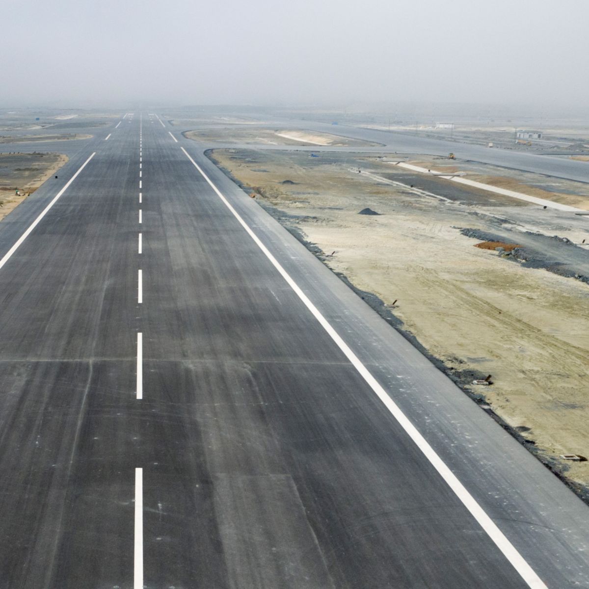 Newly paved runway surrounded by active construction and equipment zones.