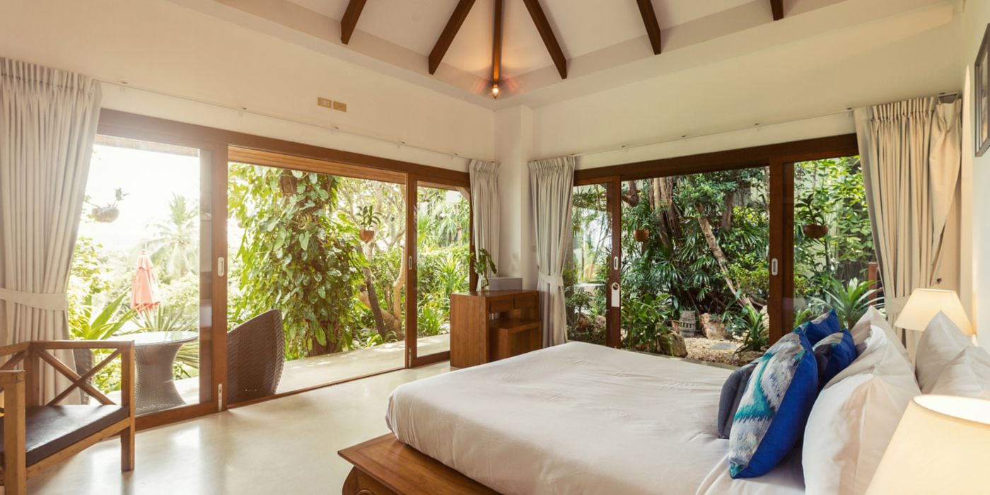 Large windows reveal lush tropical garden from spacious bedroom.