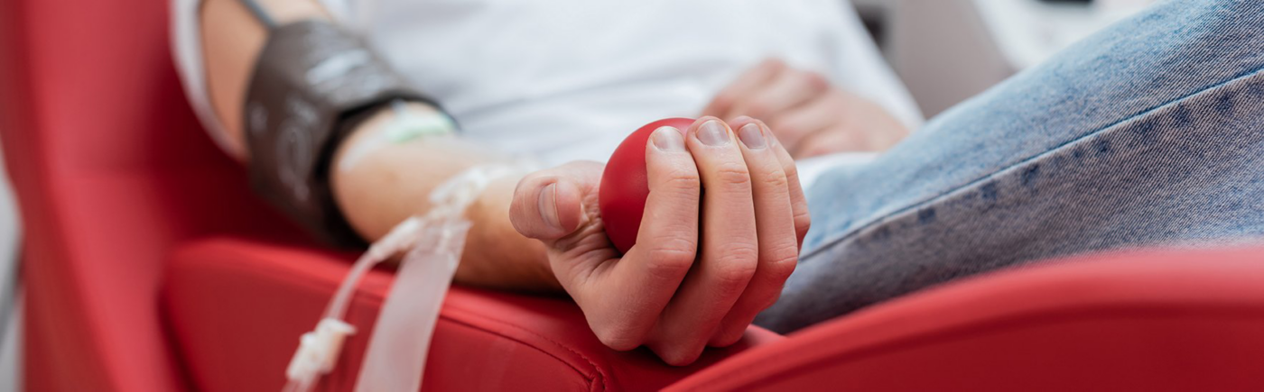 A blood donor holds a red squeeze ball while tubing rests against their arm during a donation.