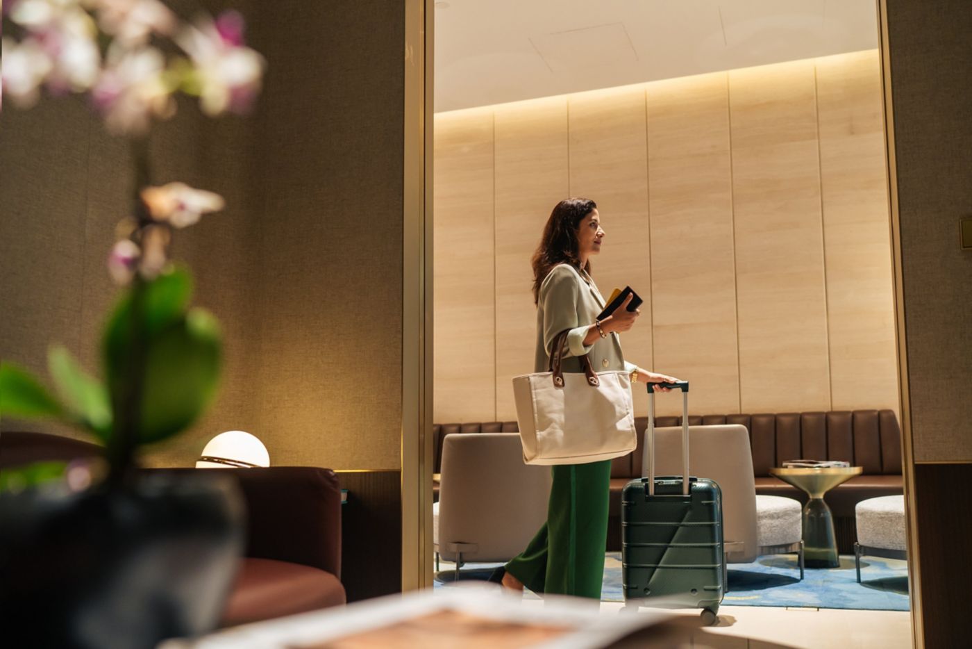 A professional woman walks through a luxury hotel lobby carrying her luggage and travel documents for check-in.