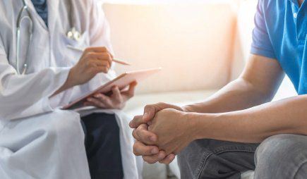 A clinician uses a tablet while speaking with a seated patient during a consultation.
