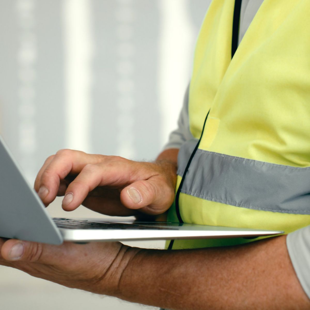 An engineer in a high-visibility safety vest works on a laptop at a construction site.