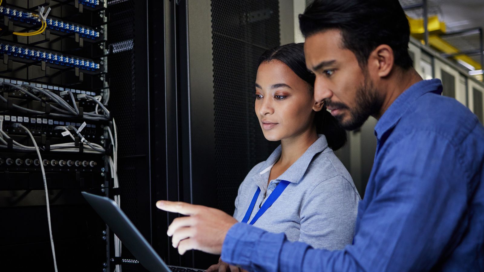 IT professionals engaged in a collaborative discussion within a data center environment. The individuals are focused on a series of server racks filled with cabling and network equipment, highlighting the intricacies of modern networking.