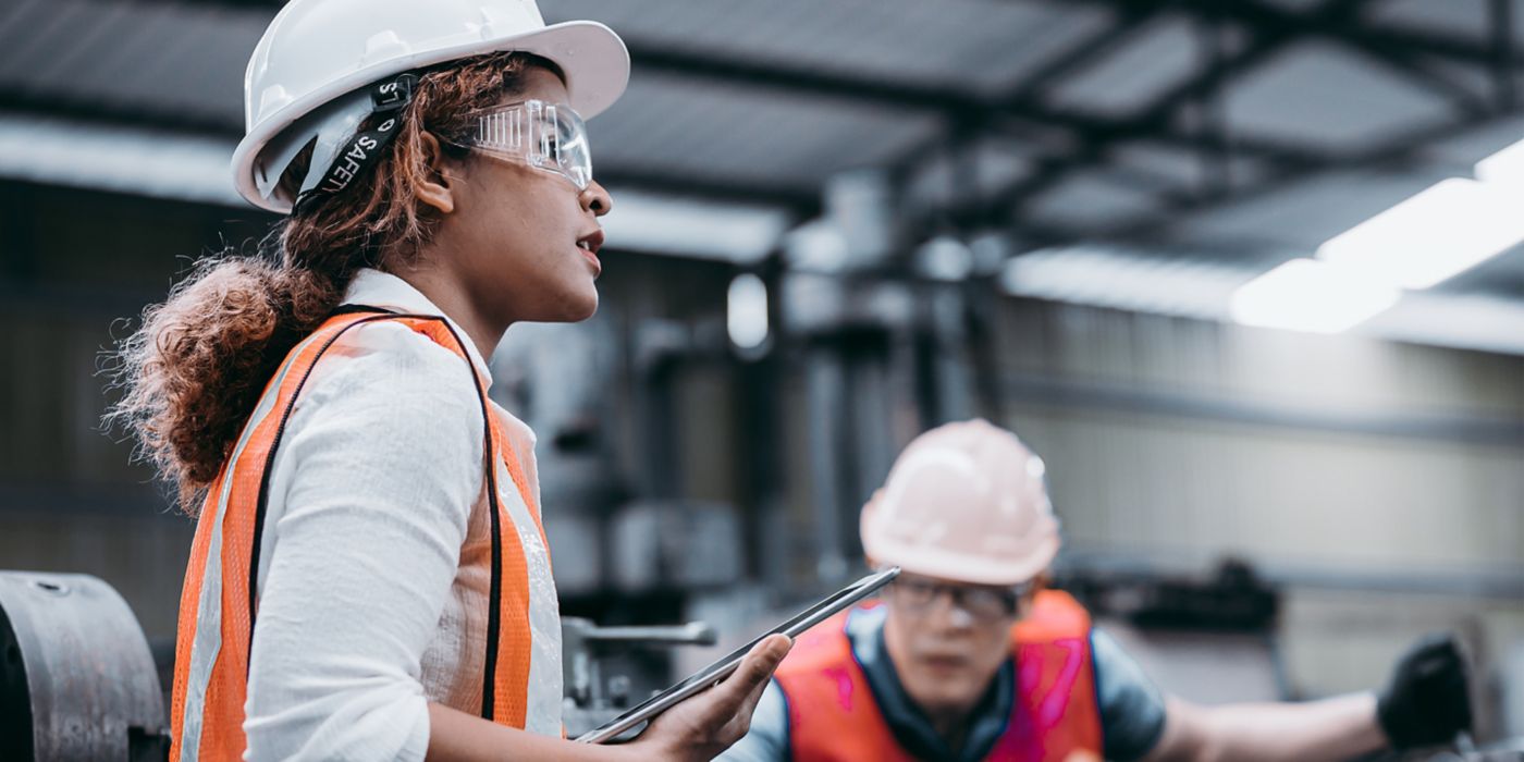 Two construction workers in safety gear, focused on their tasks in a factory environment, highlighting teamwork and safety practices.