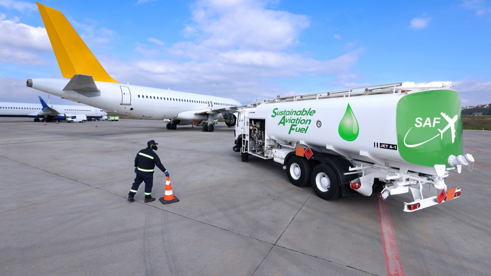 A ground crew member directs a refueling truck labeled 'Sustainable Aviation Fuel' (SAF) at an airport, showcasing eco-friendly air travel advancements.