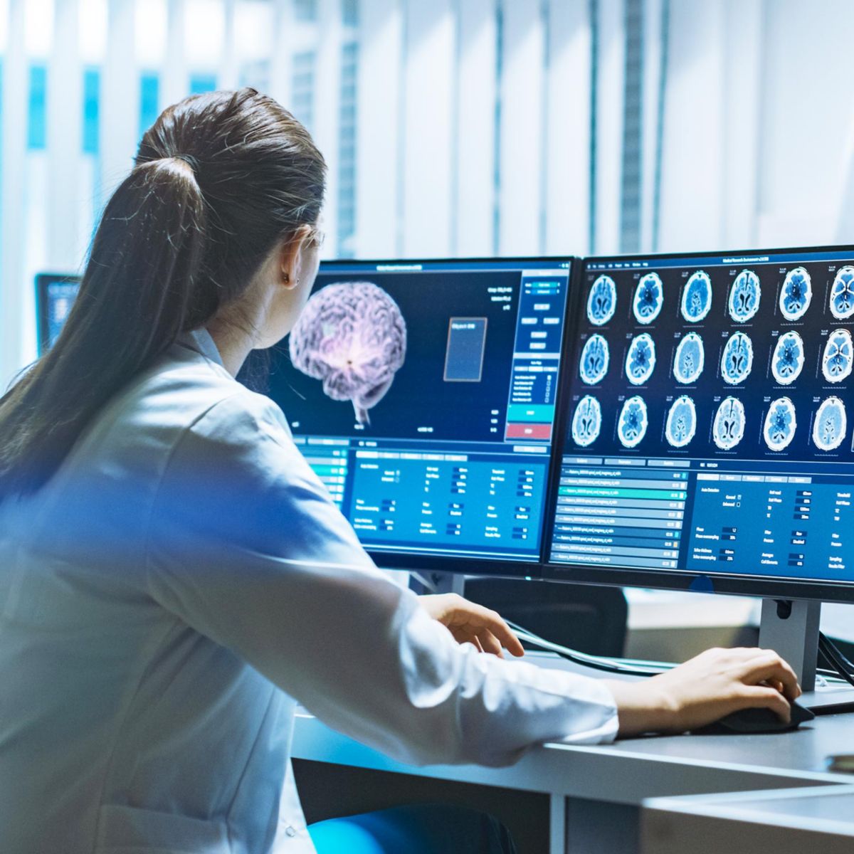 A healthcare professional analyzes brain scans on multiple monitors, showcasing advanced medical imaging technology.