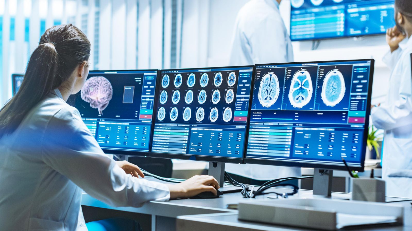 A healthcare professional analyzes brain scans on multiple monitors, showcasing advanced medical imaging technology.