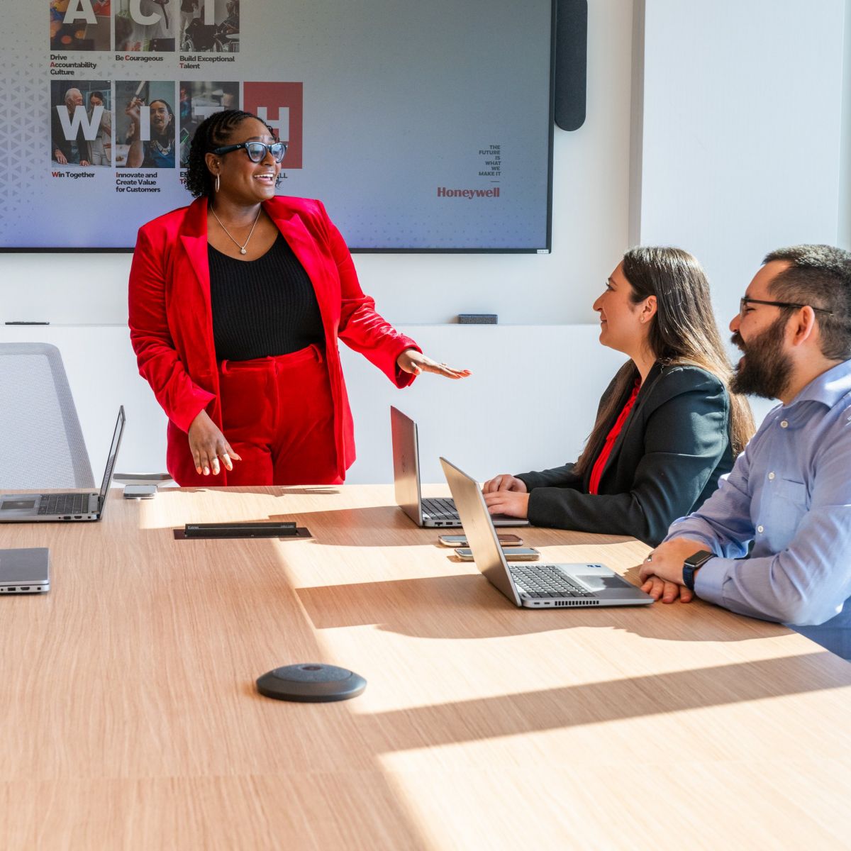 A vibrant leader in a red suit presents to a diverse professional team during a collaborative strategy session in a modern office boardroom.