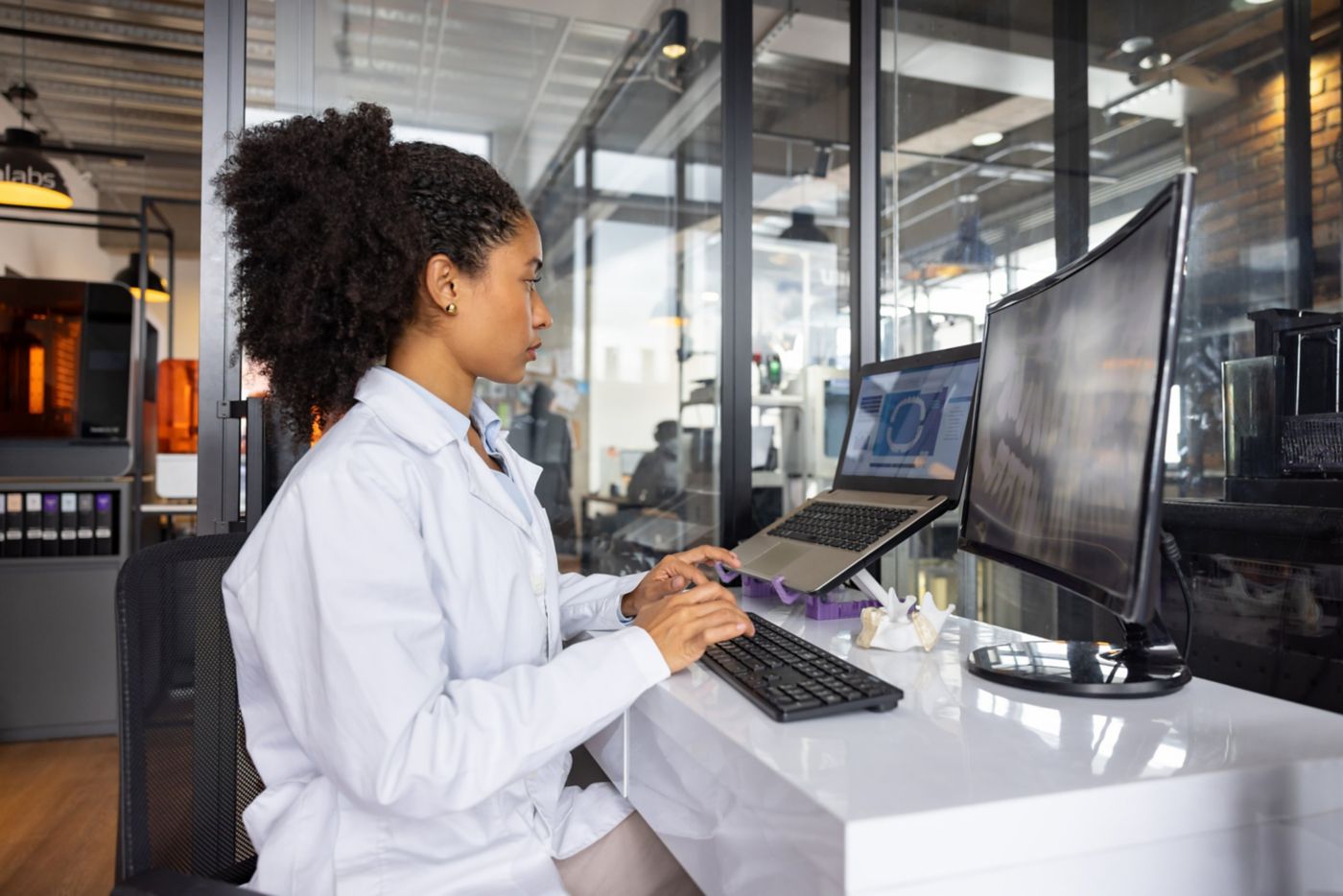 A focused technician in a modern lab uses a computer to review digital dental imaging and 3D models for precision prosthetics design.