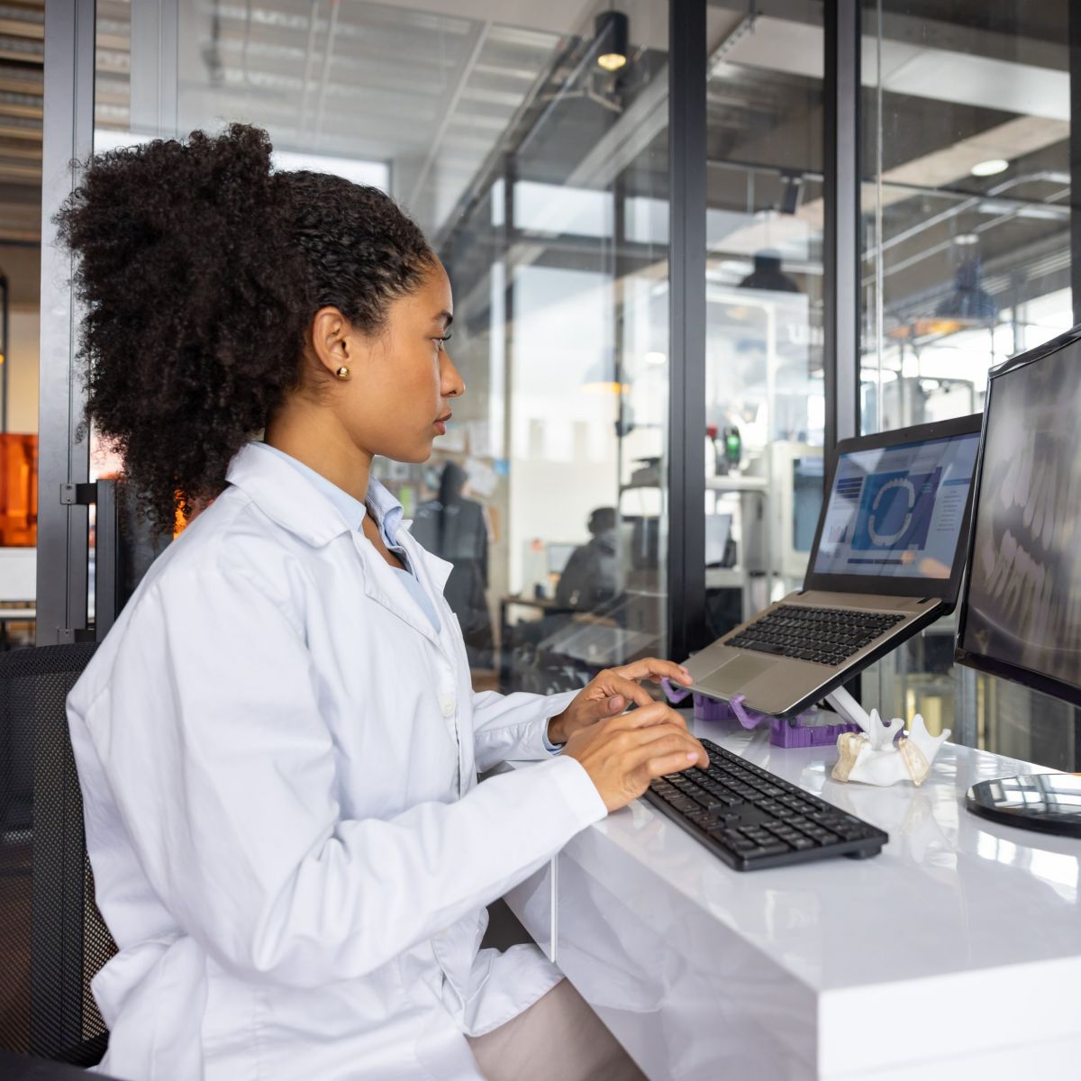 A focused technician in a modern lab uses a computer to review digital dental imaging and 3D models for precision prosthetics design.