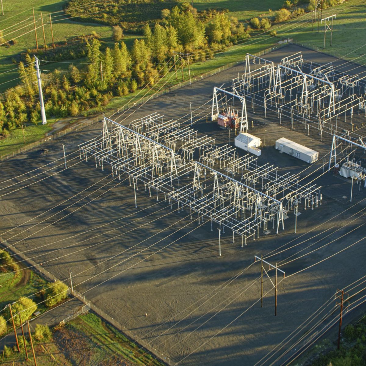 An aerial perspective of an electrical substation featuring metal framework and power lines surrounded by greenery during golden hour.