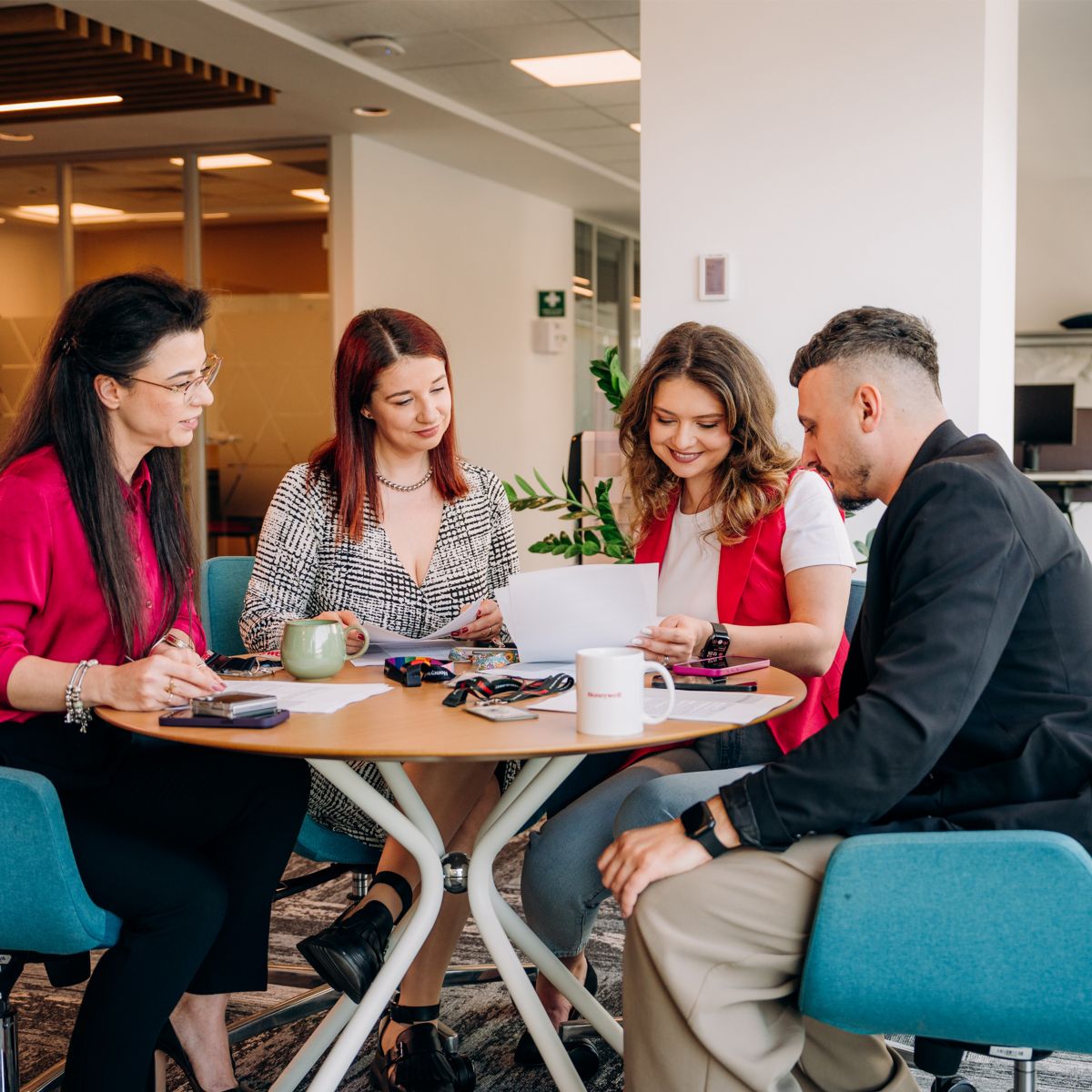 Employees in a modern office collaborate around a table, reviewing documents and discussing ideas—capturing teamwork, productivity, and a dynamic workplace environment.