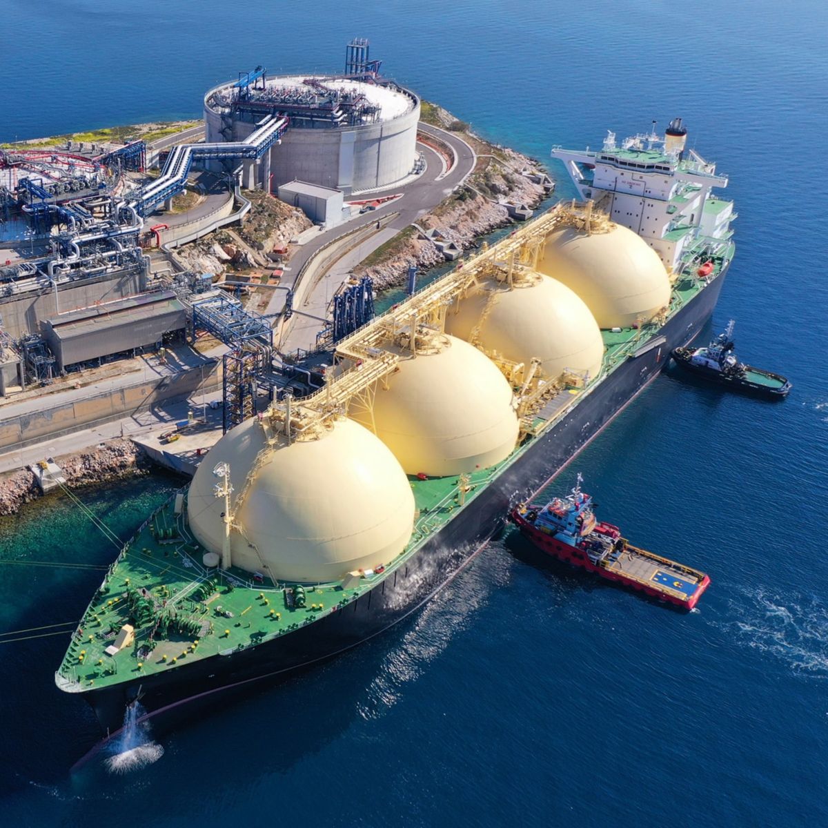 Aerial view of an LNG carrier at a coastal terminal with storage tanks, processing infrastructure and marine support vessels.