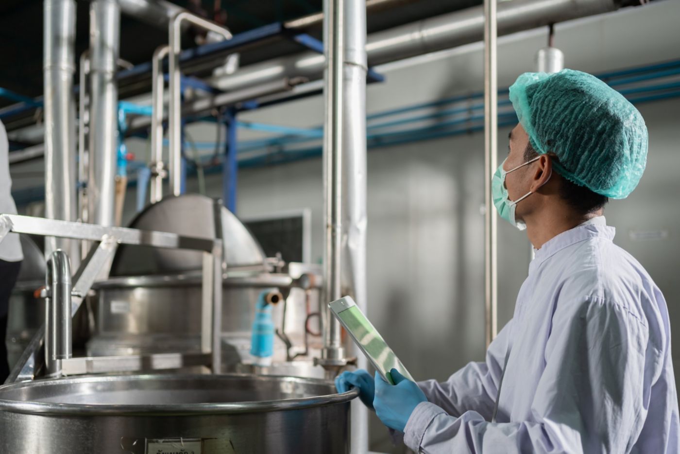 An industrial worker in protective gear uses a digital tablet to monitor production equipment in a sterile food processing facility.