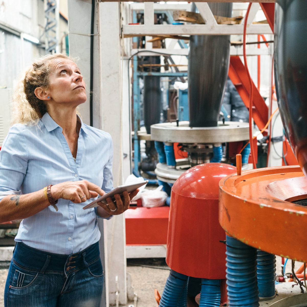 A professional female engineer uses a tablet to inspect industrial manufacturing equipment in a factory setting.