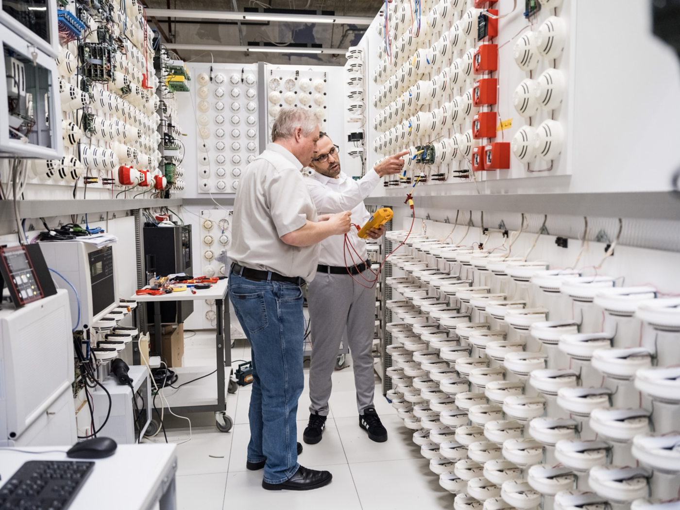 Engineers testing and configuring smoke detectors in a fire safety lab environment.