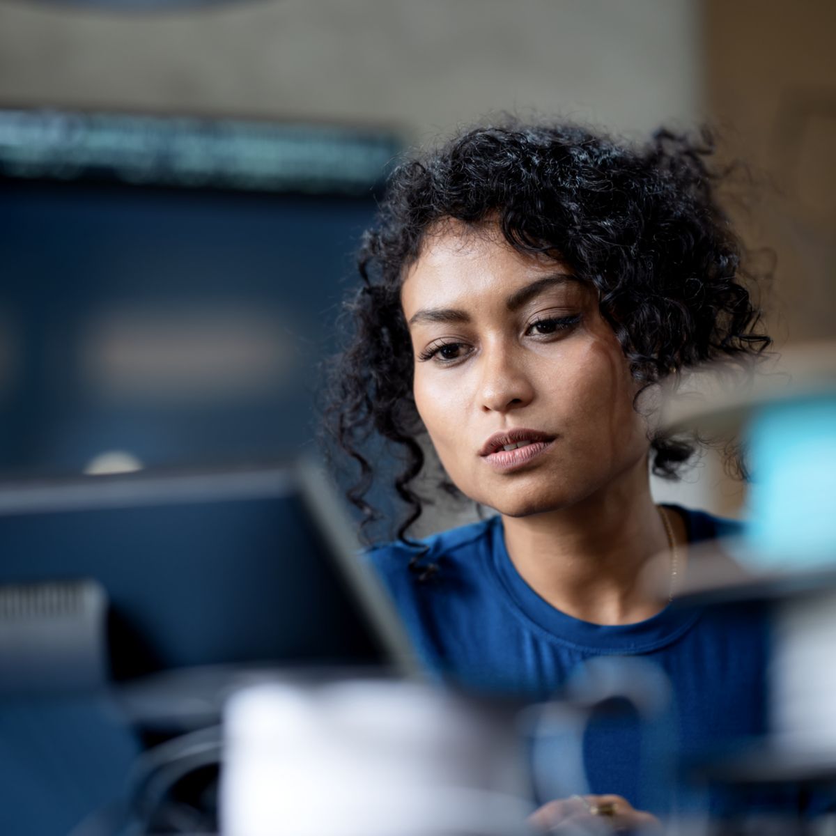A person with curly hair is focused on their work at a computer in a contemporary office setting.