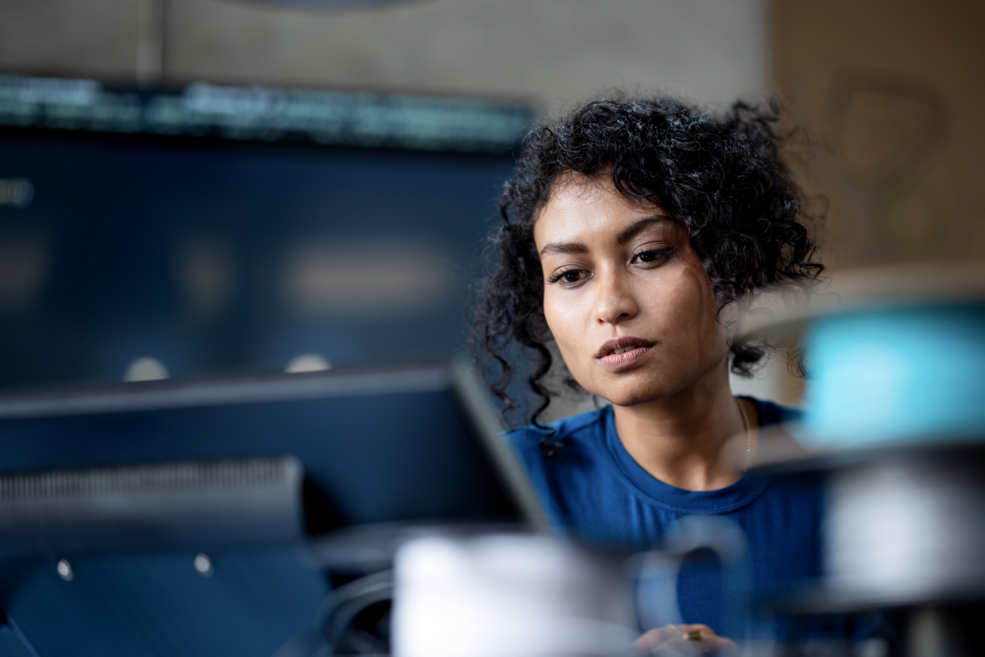 A person with curly hair is focused on their work at a computer in a contemporary office setting.