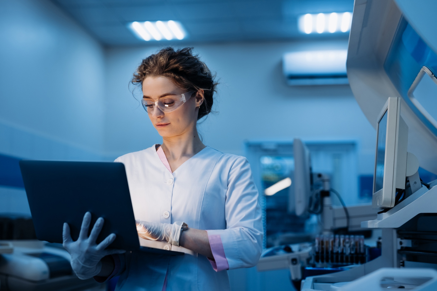 A healthcare worker in scrubs and gloves focuses on a laptop in a modern clinic, showcasing the vital role of technology in medical practice.