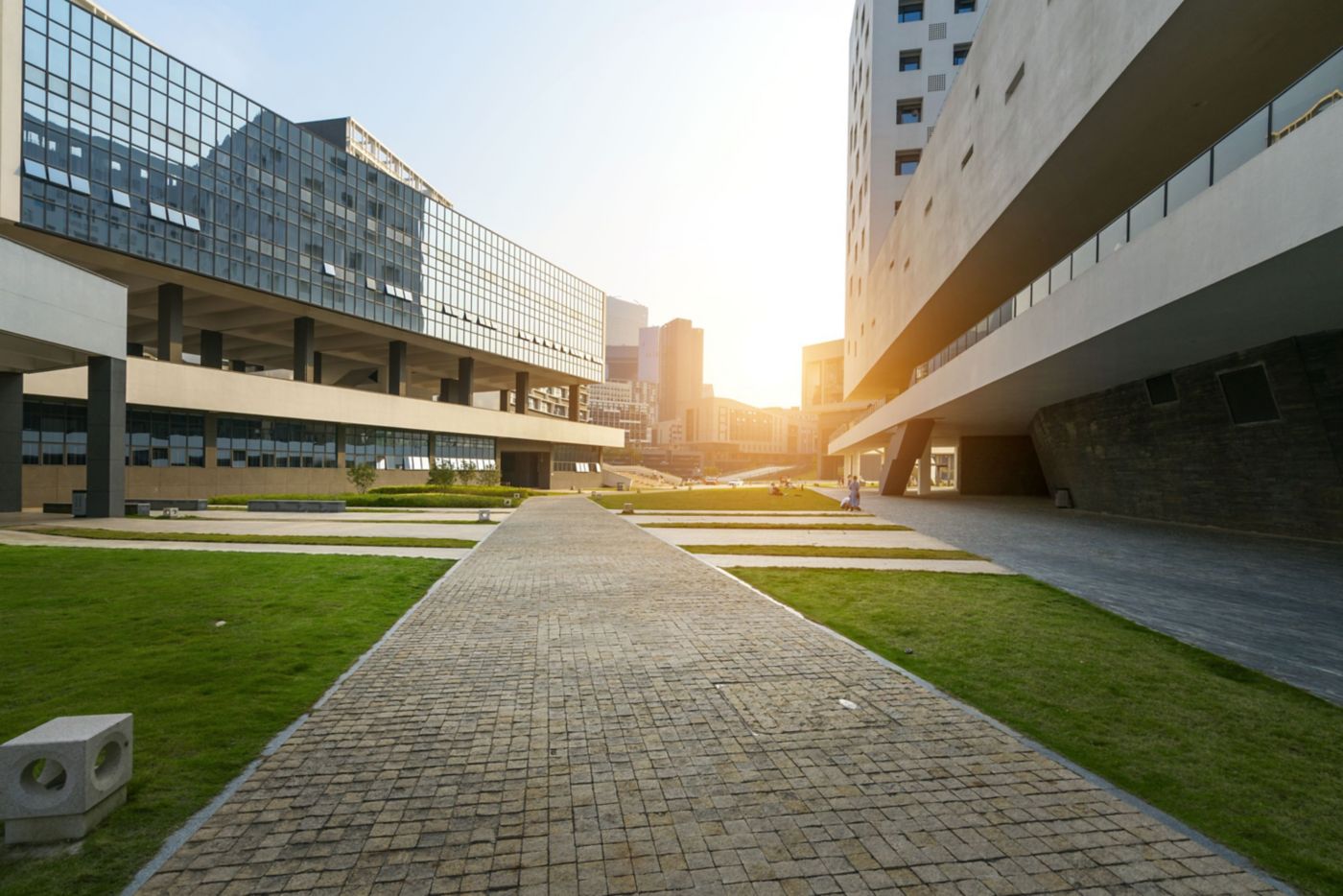  modern architectural scene with sleek buildings, paved pathways, and lush lawns, illuminated by the warm glow of the setting sun.