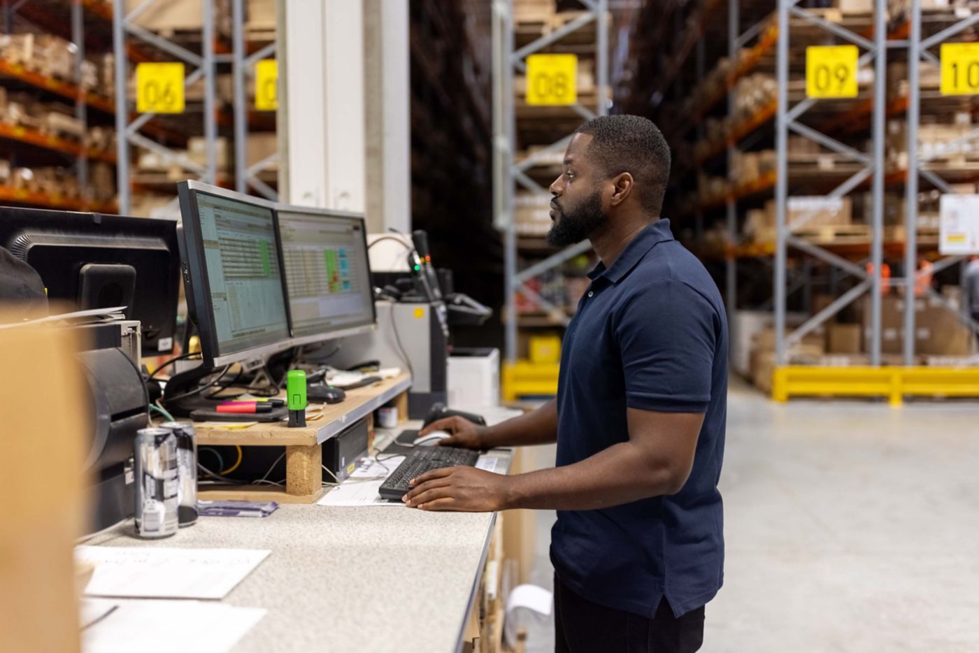 Side view of african male worker working on computer in a distribution warehouse. Man working on computer in large factory warehouse.