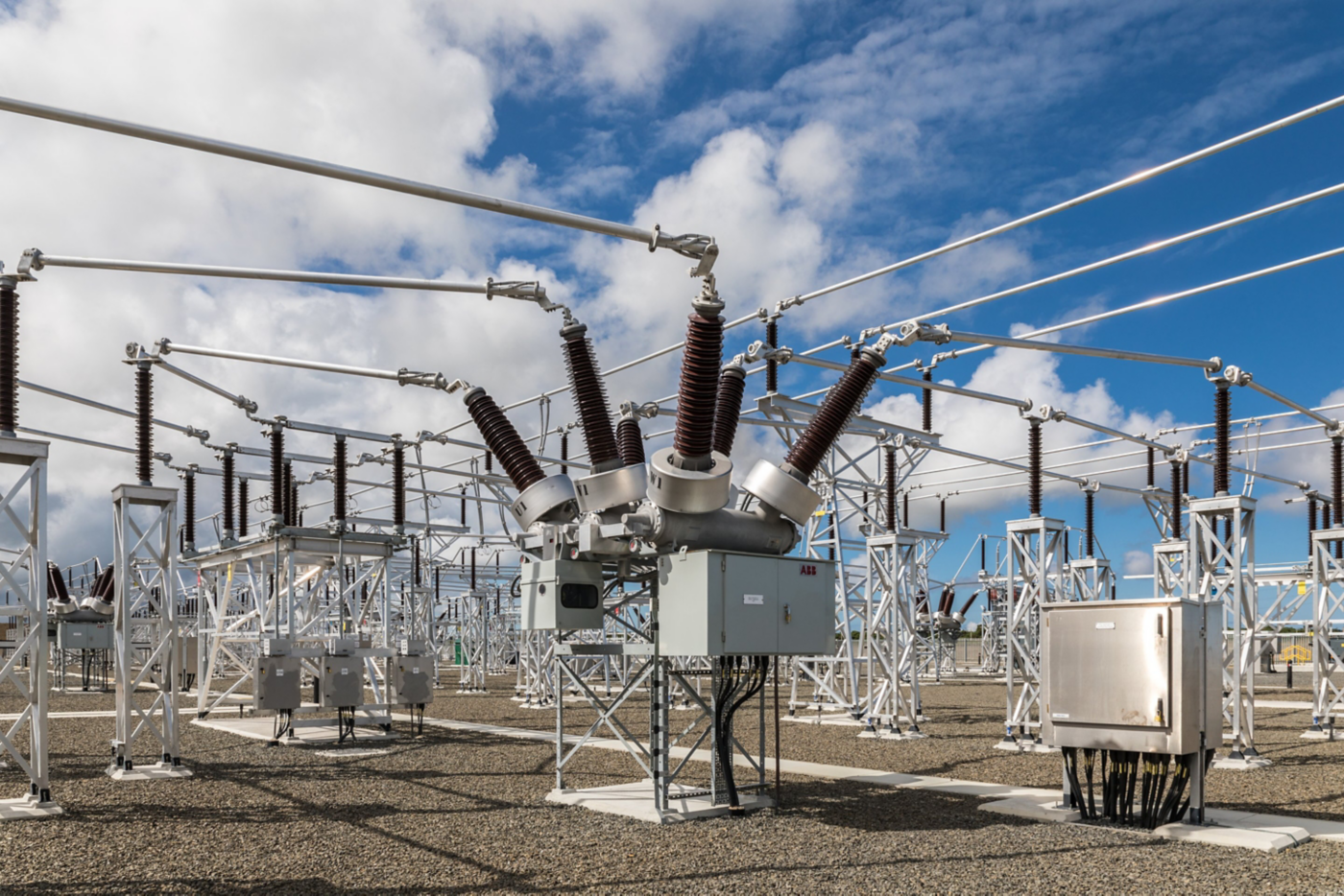 Industrial view of high voltage electrical equipment and transmission infrastructure under a bright blue sky with scattered clouds.
