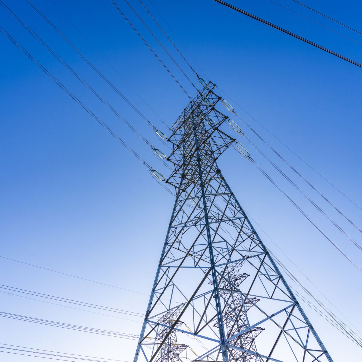 Low-angle view of a metallic electricity transmission pylon reaching into a clear blue sky.