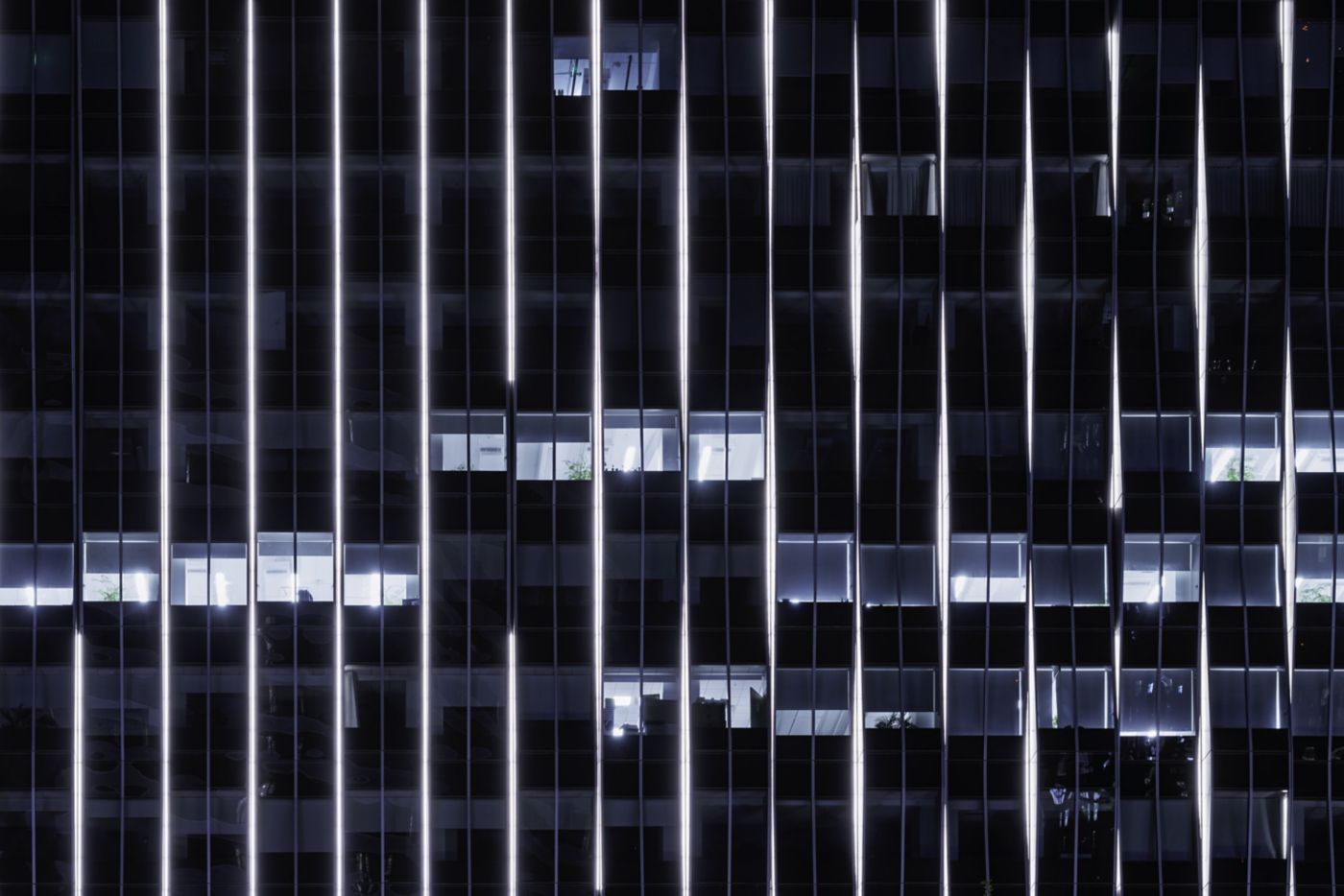 Vertical light strips emphasize the architectural grid of a modern high-rise office building during the night.