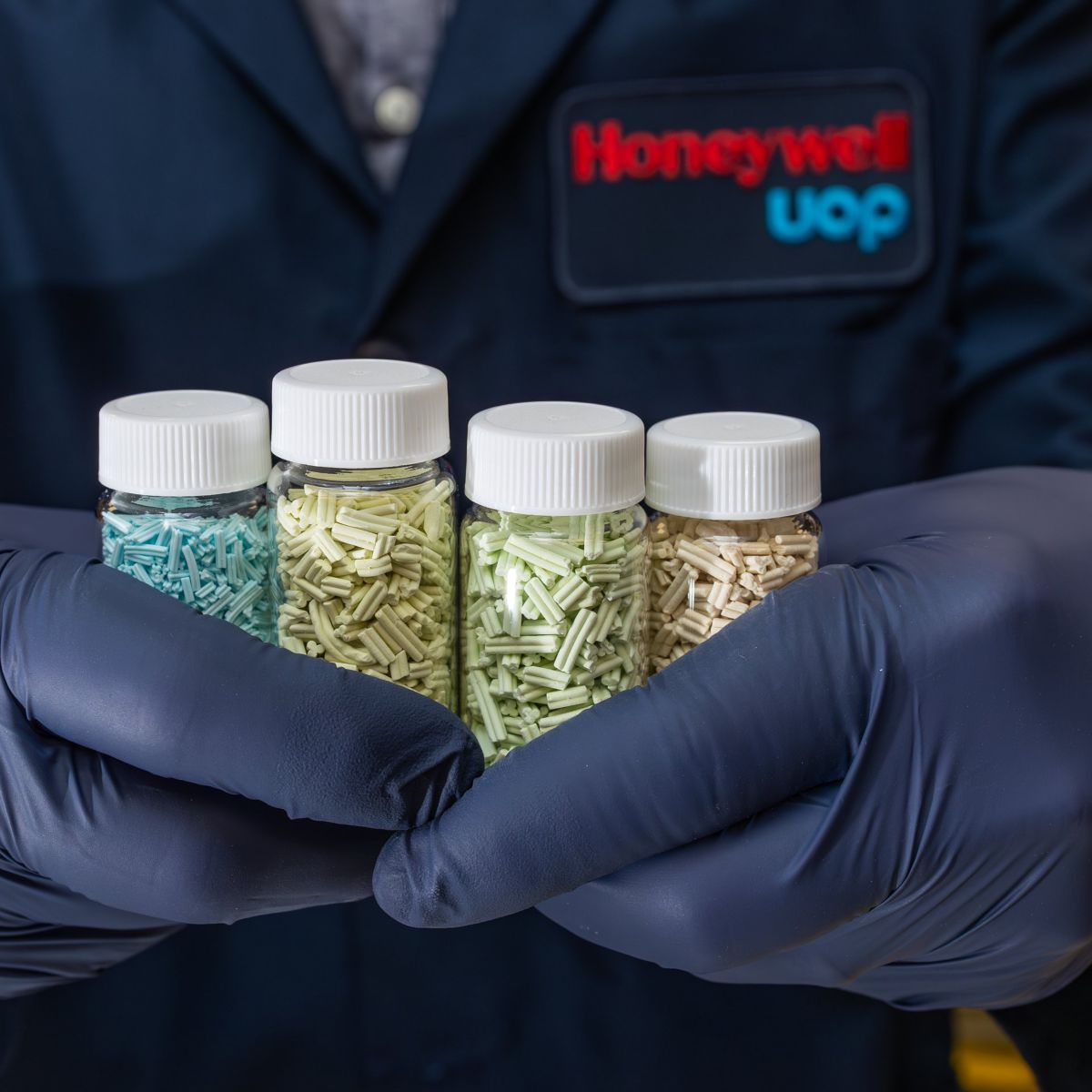 A laboratory technician holds four vials containing various multi-colored industrial catalyst pellets for chemical processing research.