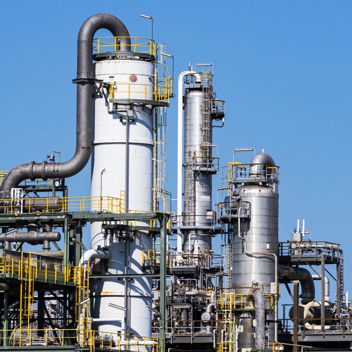 Steel distillation columns and pipelines stand against a clear blue sky in this industrial refinery facility.