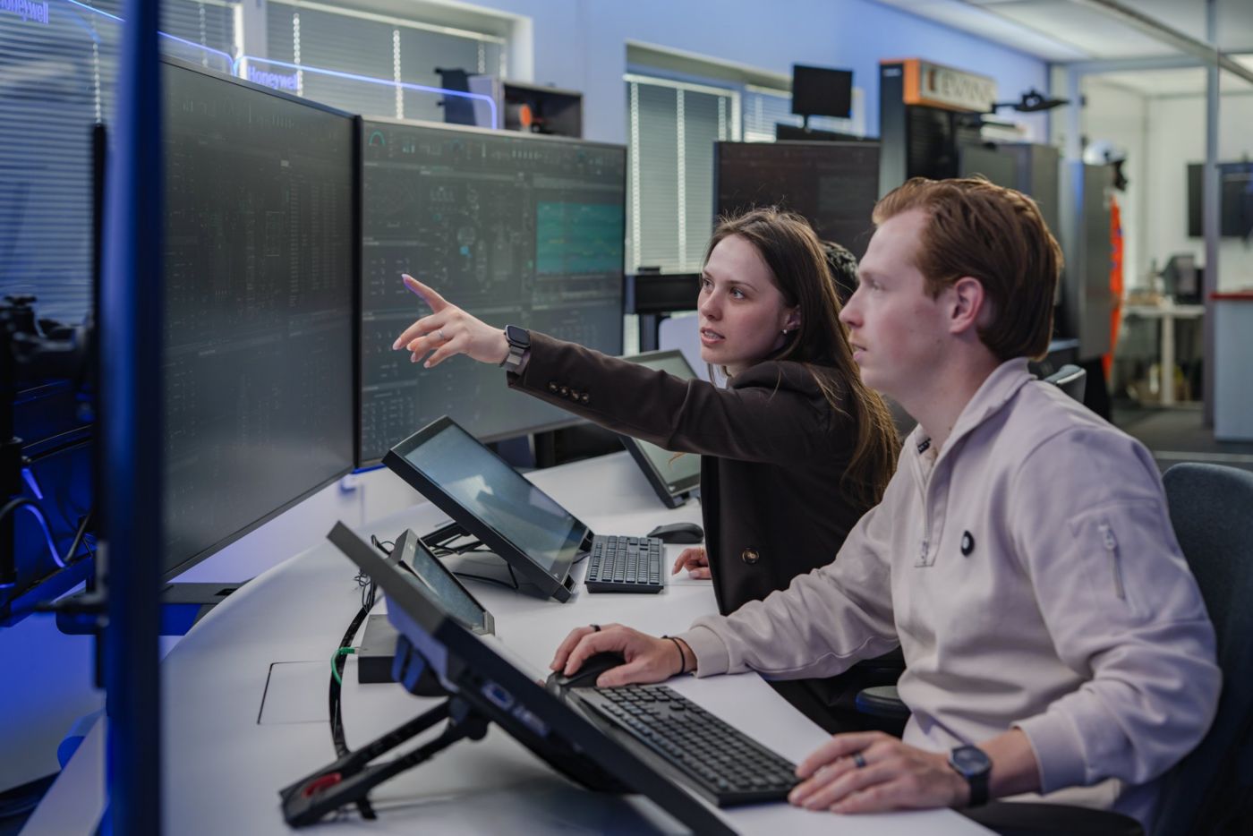 Technicians collaborate while monitoring complex industrial data streams on large digital screens in a modern corporate control room environment.