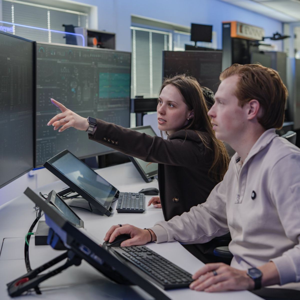 Technicians collaborate while monitoring complex industrial data streams on large digital screens in a modern corporate control room environment.