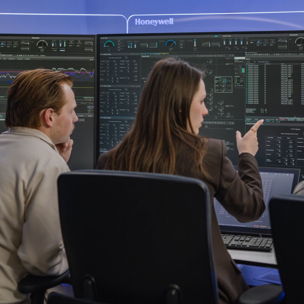 A team of engineers collaborates in a high-tech Honeywell control room, analyzing complex industrial data displays on a multi-screen workstation.