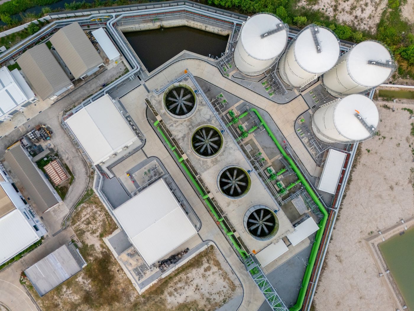 An aerial top-down view shows the cooling towers, storage tanks, and interconnected piping infrastructure of a modern industrial complex.