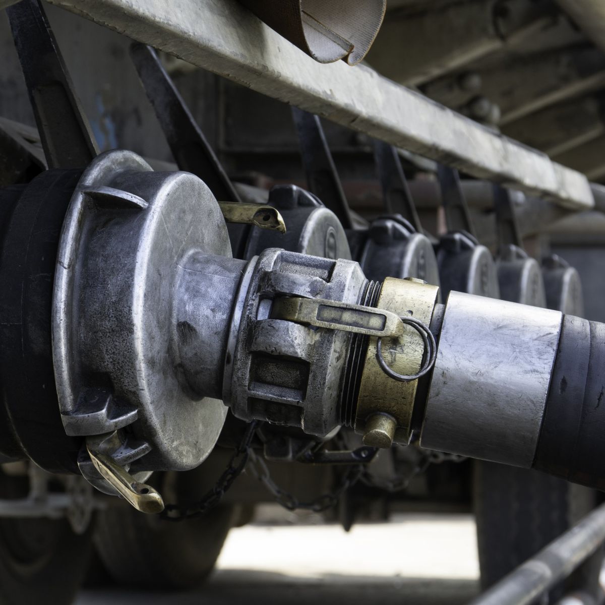 A close-up shot showing a thick, black industrial hose securely connected to the heavy-duty metal valve system of a commercial tanker truck.