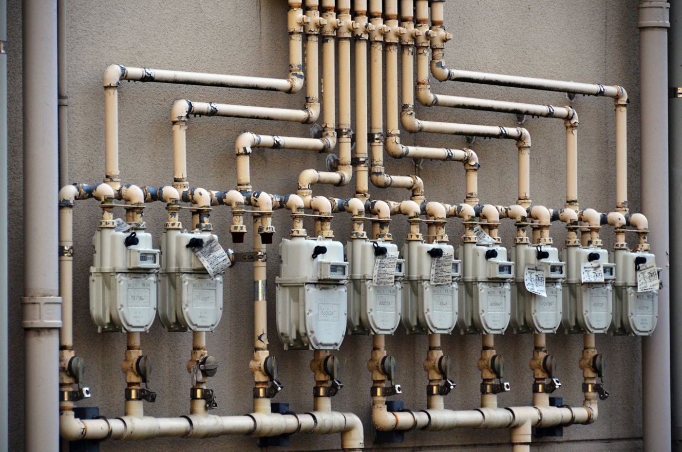 A series of industrial gas meters with interconnected piping mounted on an exterior wall.
