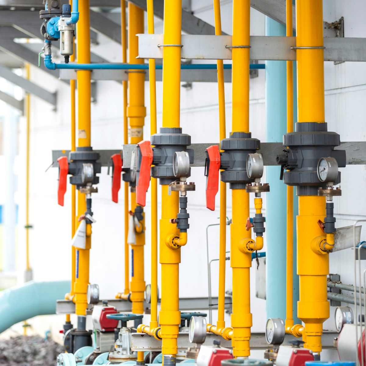 Industrial yellow piping and valve systems with gauges mounted on an exterior wall at a processing facility.