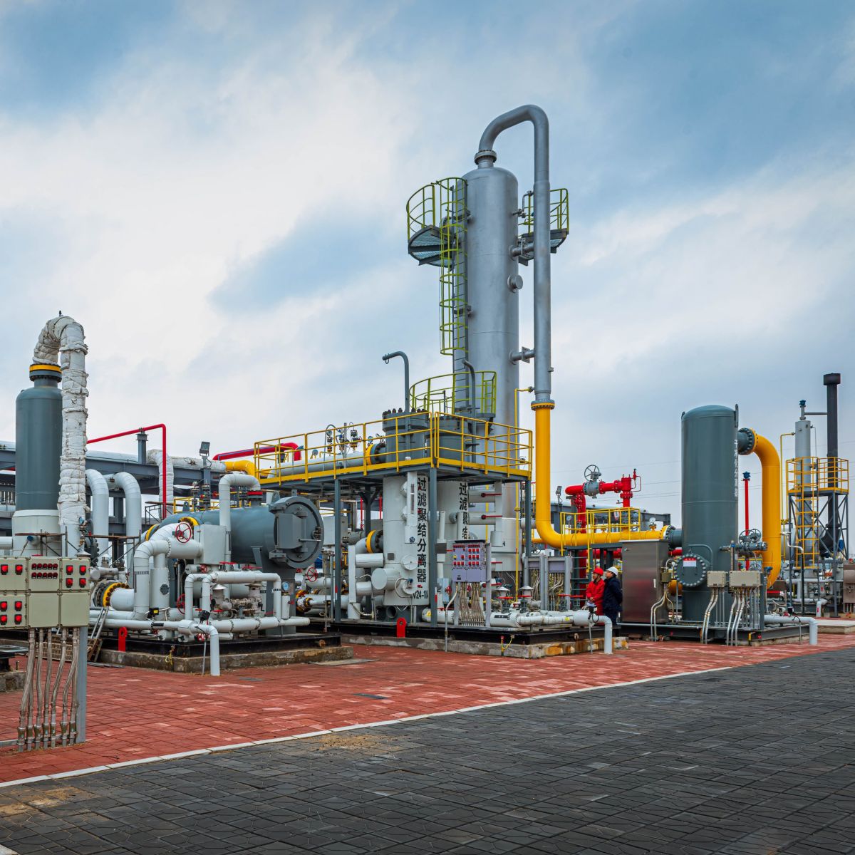 Wide-angle view of a modern natural gas processing plant featuring complex piping networks and industrial vessels under a cloudy sky.