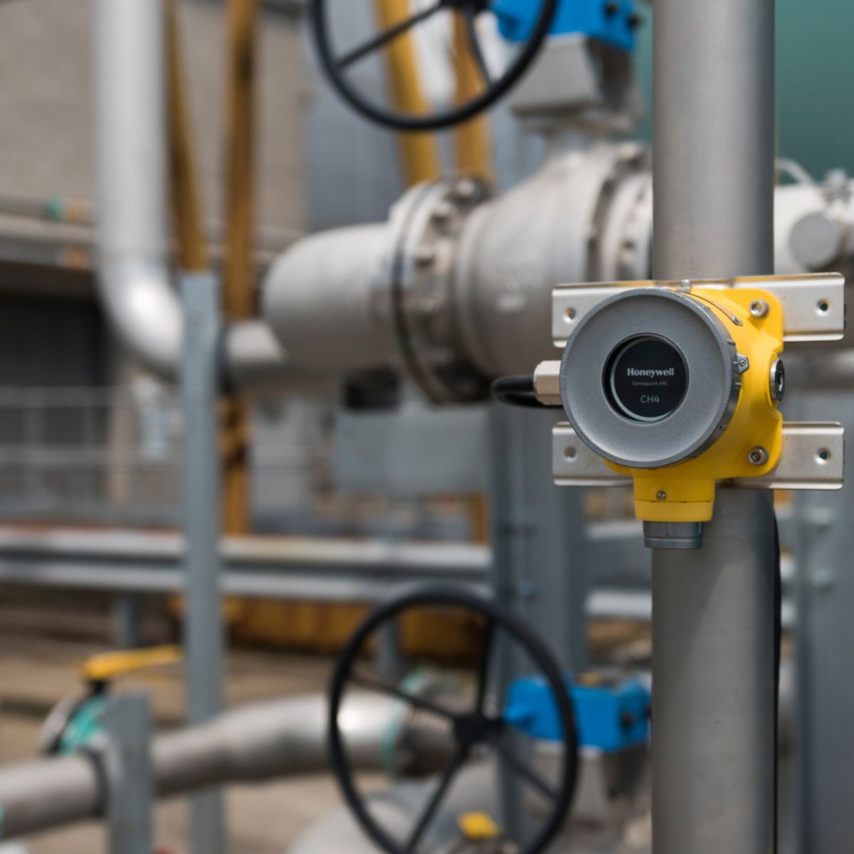A yellow Honeywell methane gas detector mounted on industrial piping within a plant.