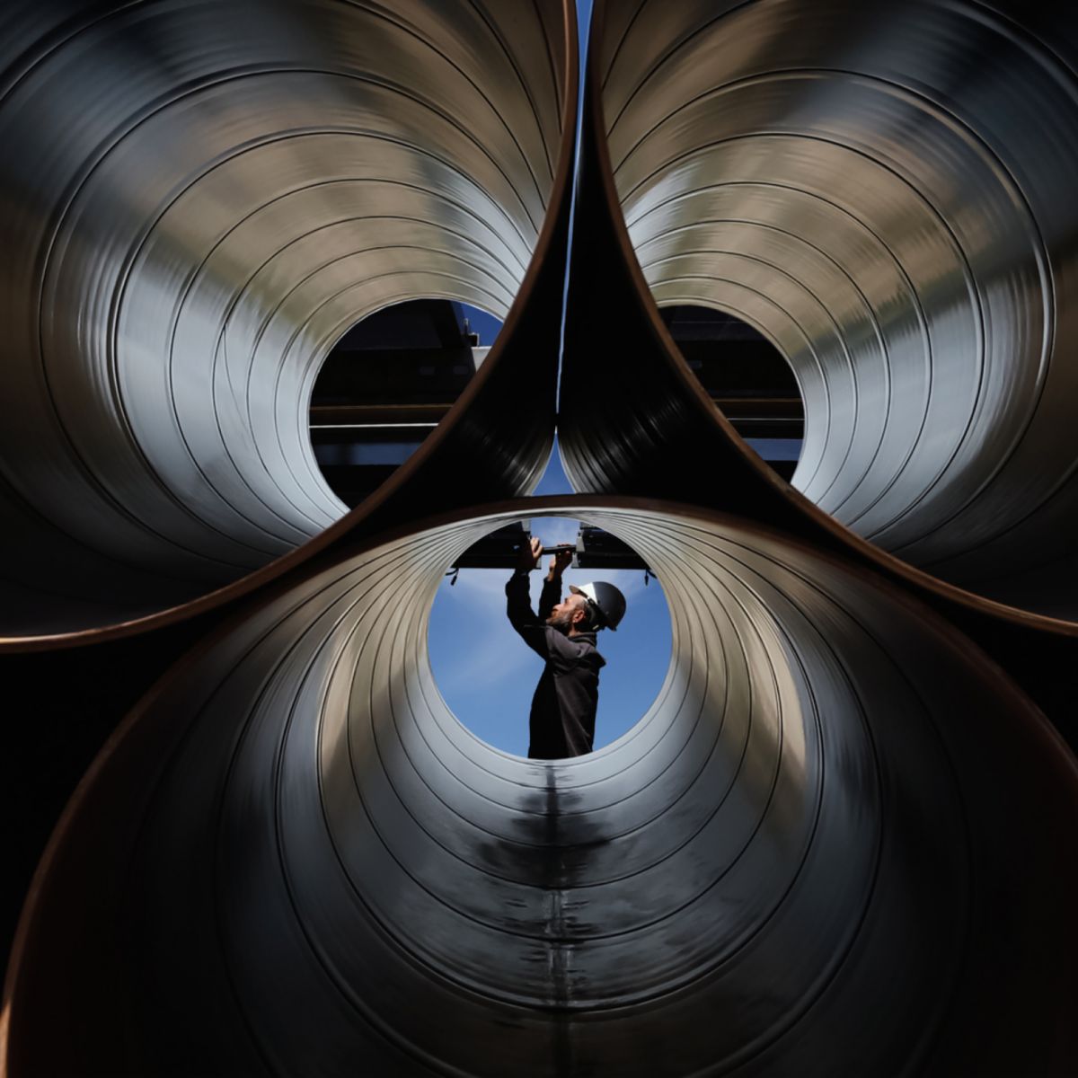 Worker inspecting large industrial pipes, representing heat transfer systems, energy efficiency, and advanced mechanical engineering solutions.