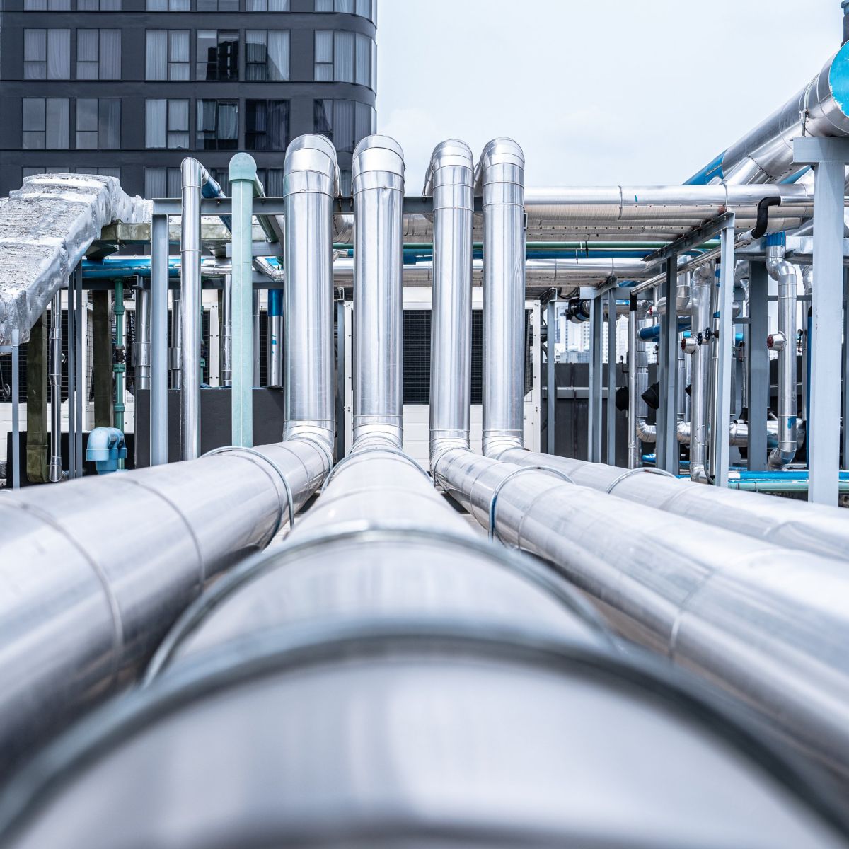 Low-angle view of insulated industrial piping systems installed on a commercial building rooftop for climate control and ventilation.