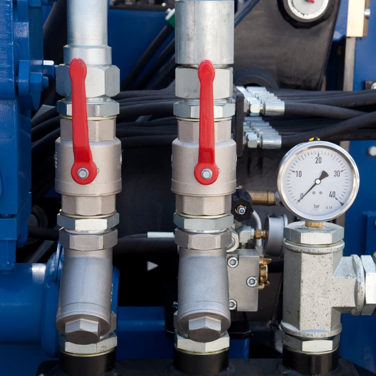 Close-up of industrial machinery featuring red-handled ball valves and a pressure gauge mounted on a blue hydraulic system manifold.