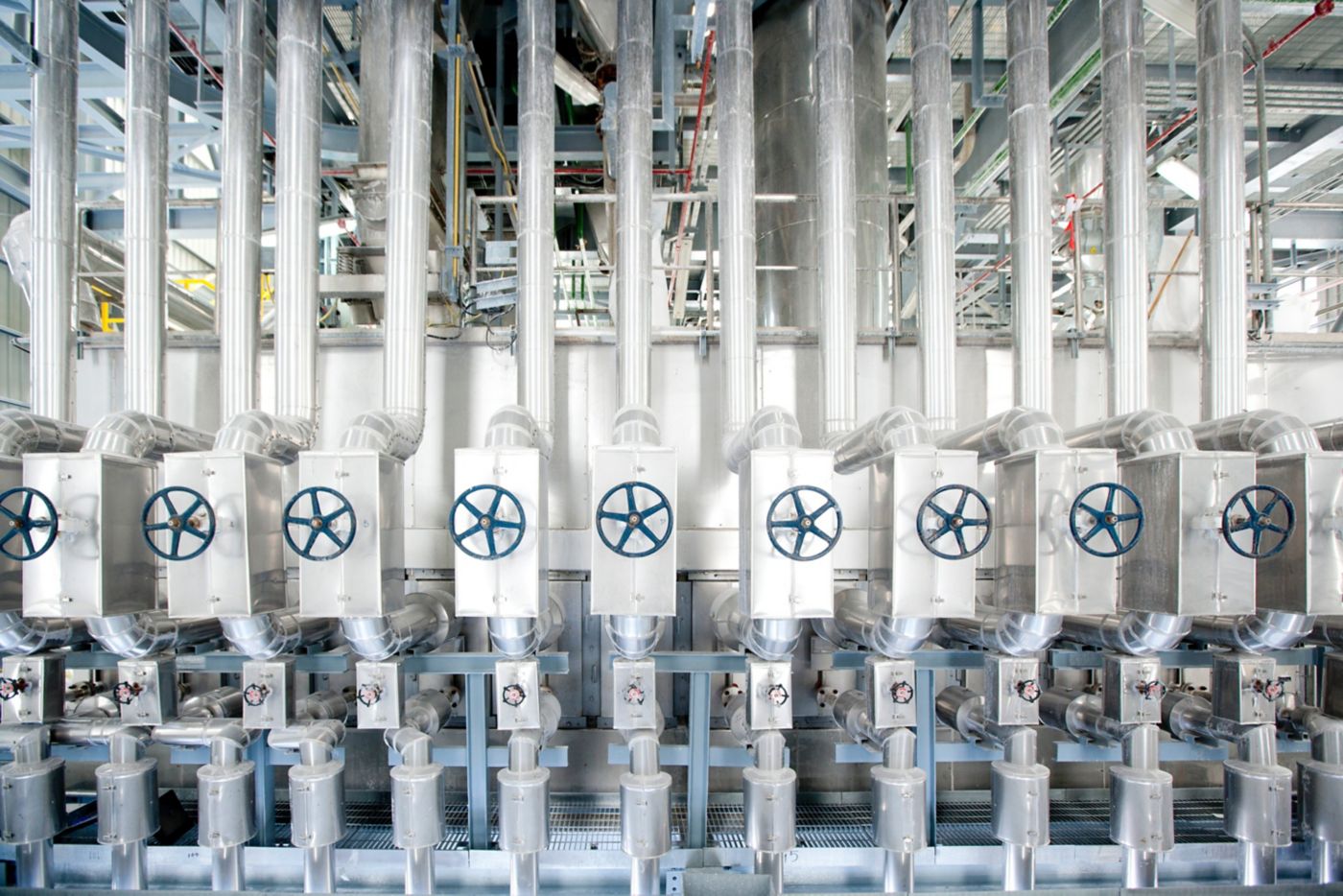A symmetrical view of industrial pipes and valve wheels in a chemical manufacturing facility.